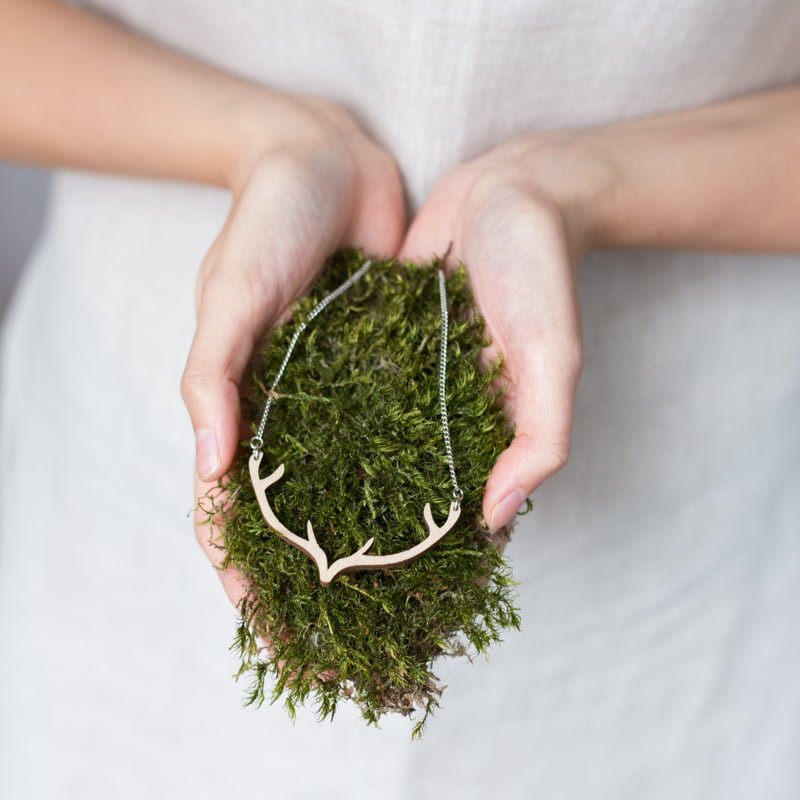 Antler swing shaped necklace on moss held by woman