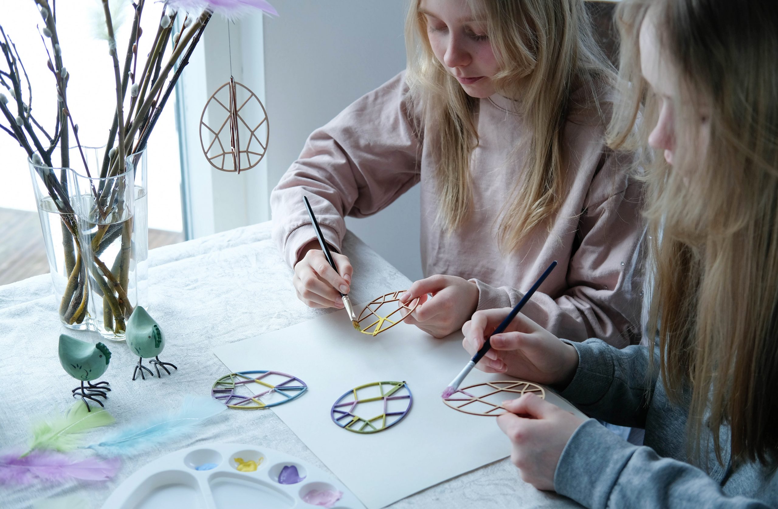 Kaksi tyttöä maalaavat pääsiäismunakoristeita pastelliväreillä