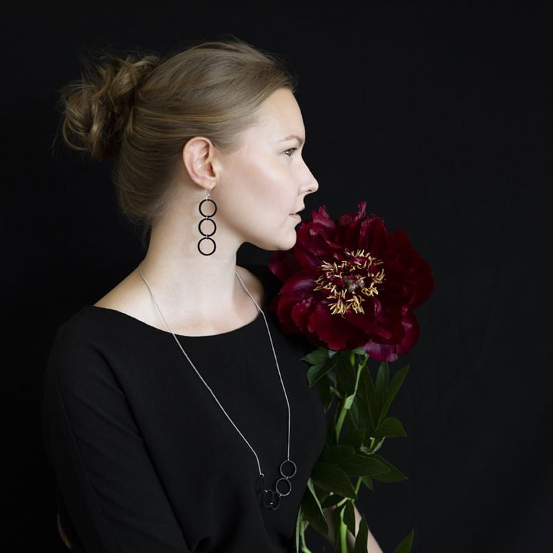 Woman in black wearing wooden black statement earrings and holding a burgundy flower