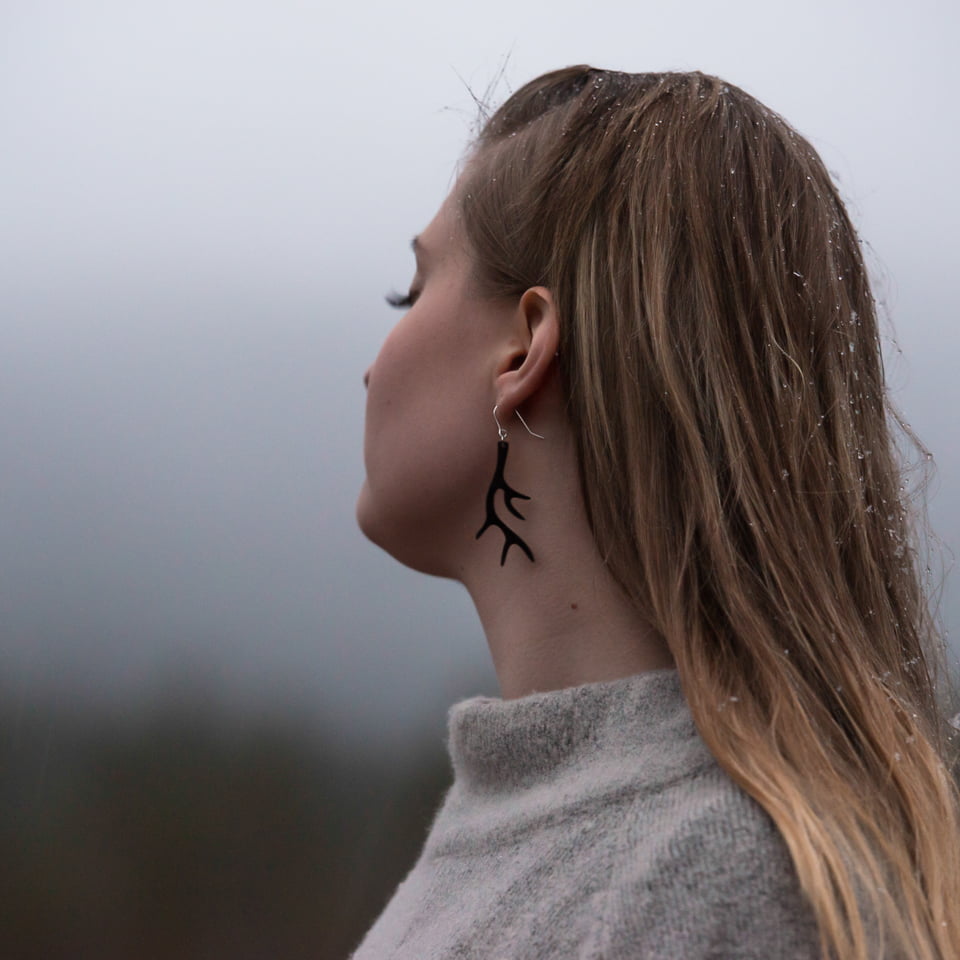 Woman standing eyes closed with big black antler earrings