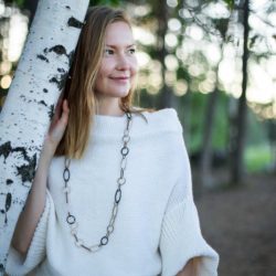 nordic woman in white leaning in birch tree wearing wooden chain necklace