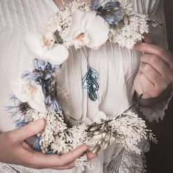 Nainen pitää kädessään kukkaseppelettä keskellä sininen puukoru