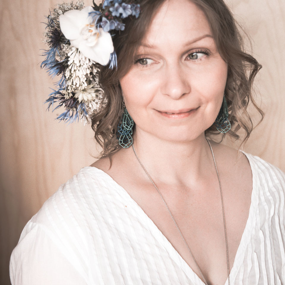Nainen valkoisissa sinivihreät puukorvakorut ja kukkaseppele