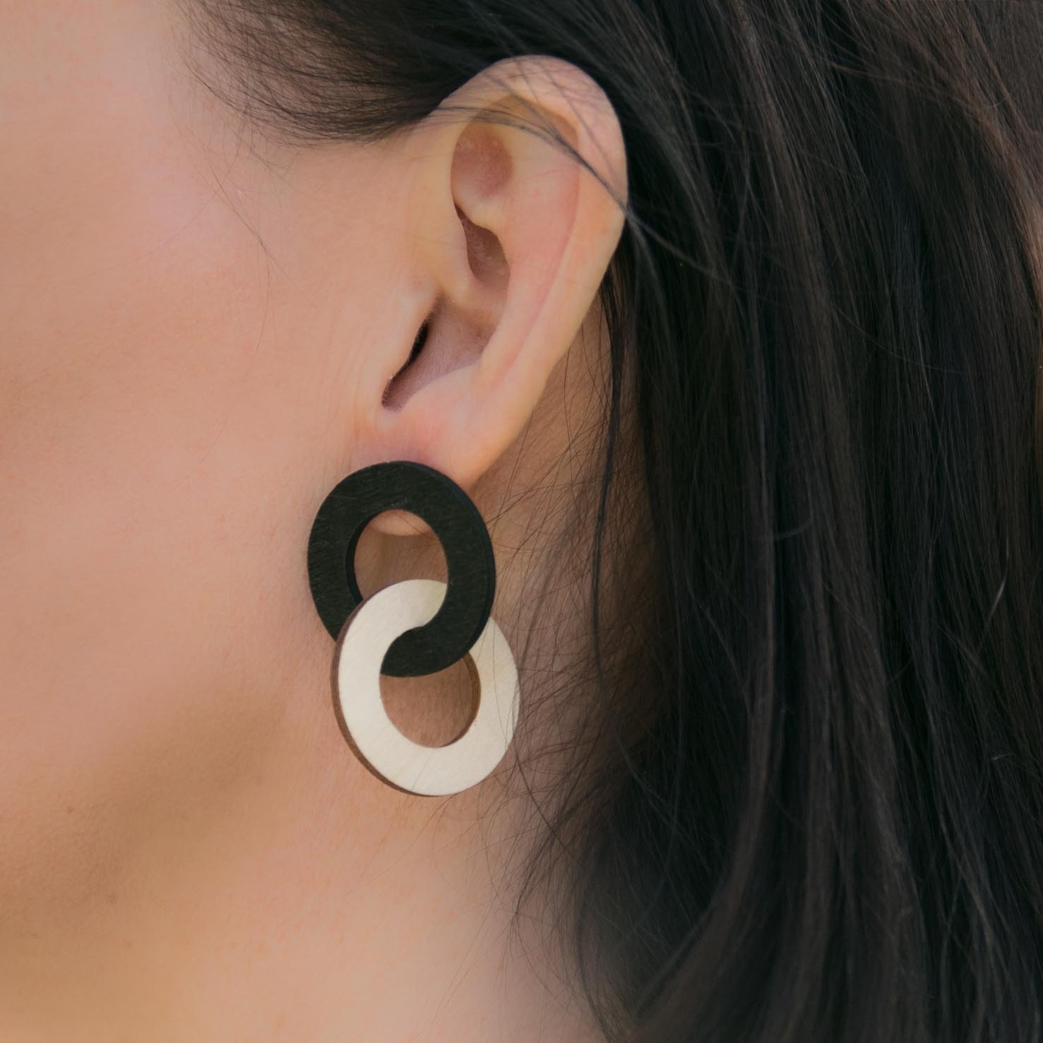 Puiset ketjukorvakorut puun ja mustan väreissä naisen korvalla