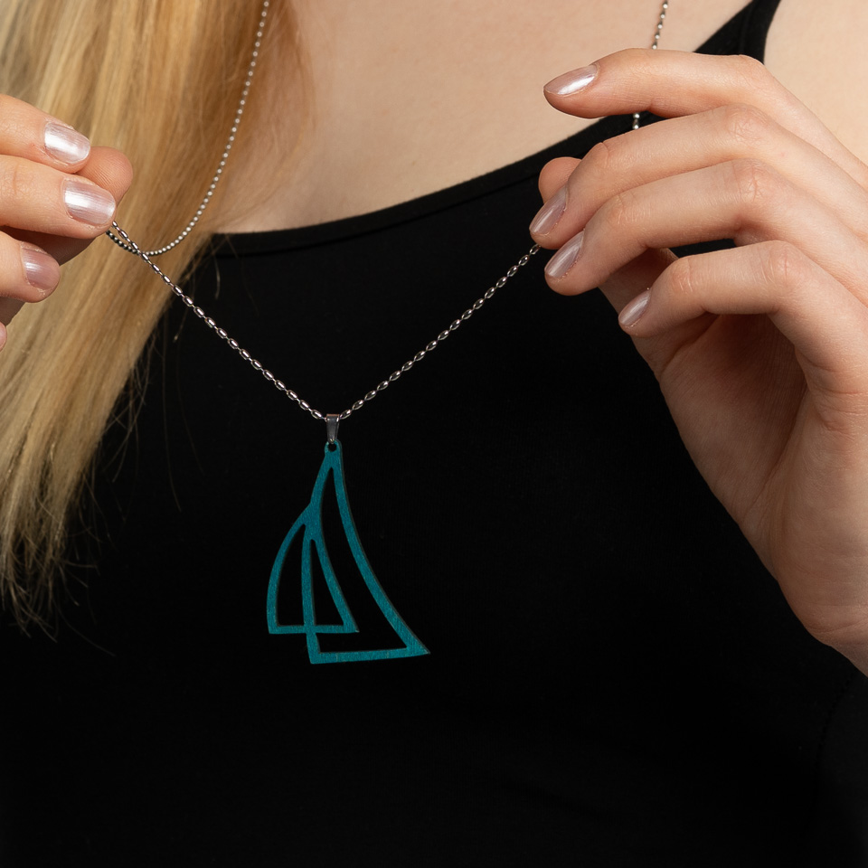 Kädet pitelevät turkoosin väristä purjevenekorua