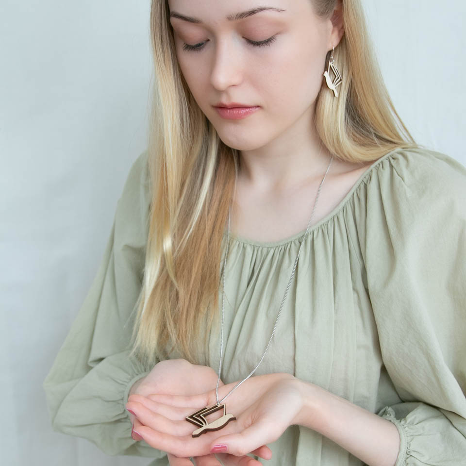 Vaaleahiuksinen nainen pitää kädessään kirjalintu -kaulakorua