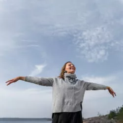 Woman spreading her arms as to fly, laughing, green stud earrings and hoop necklace