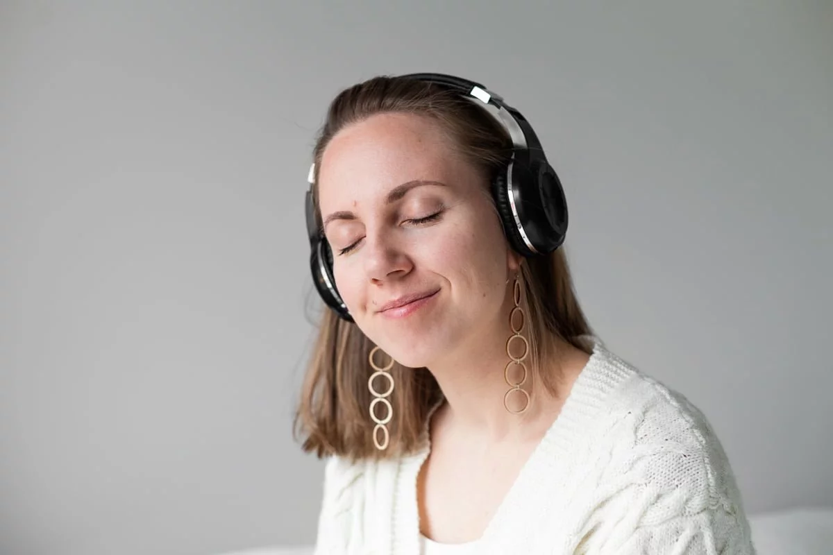 Nainen, jolla on puukorvakorut, kuuntelee kuulokkeista musiikkia silmät kiinni